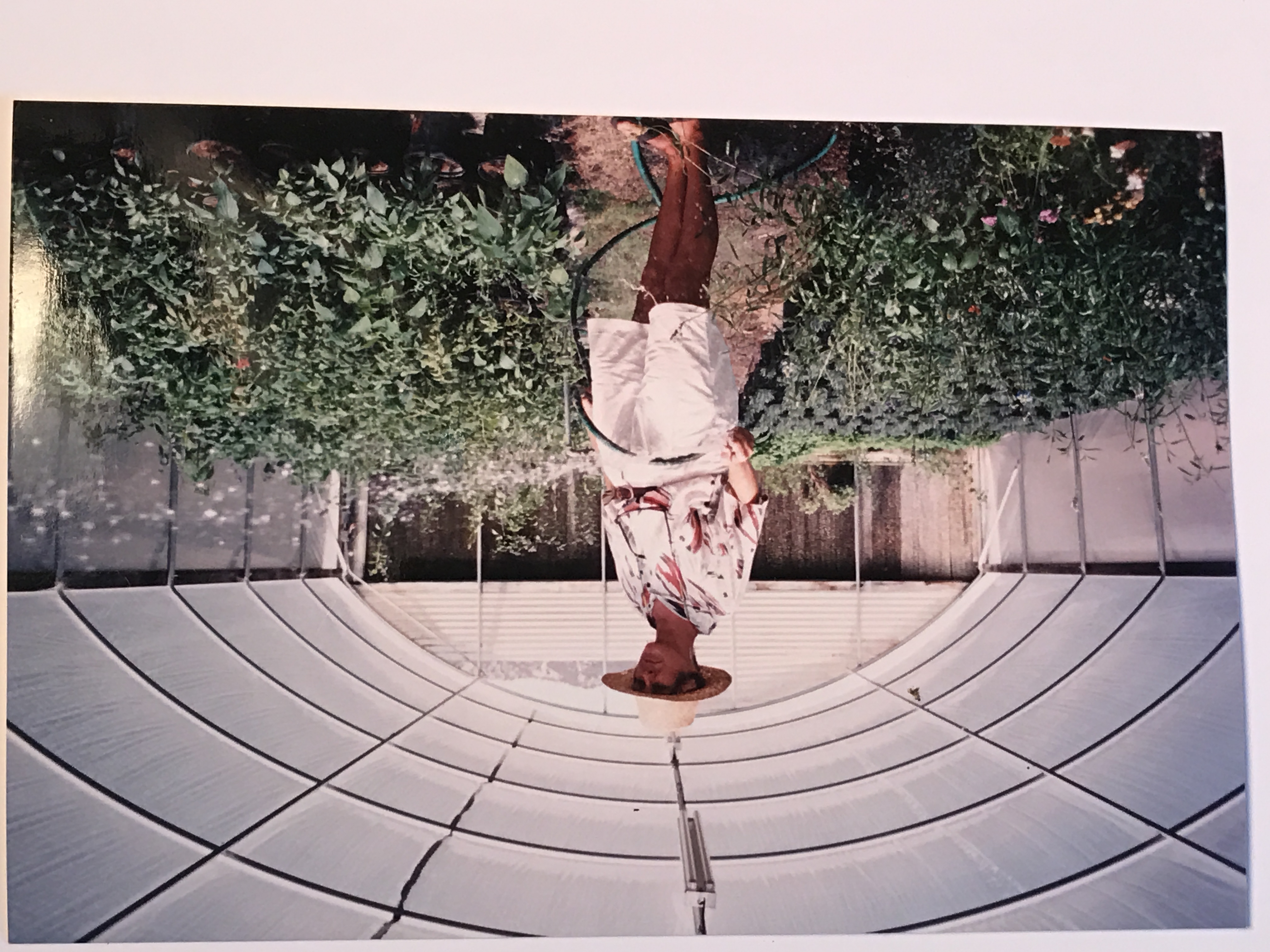Person in floral dress and hat standing beneath curved white tunnel with green foliage