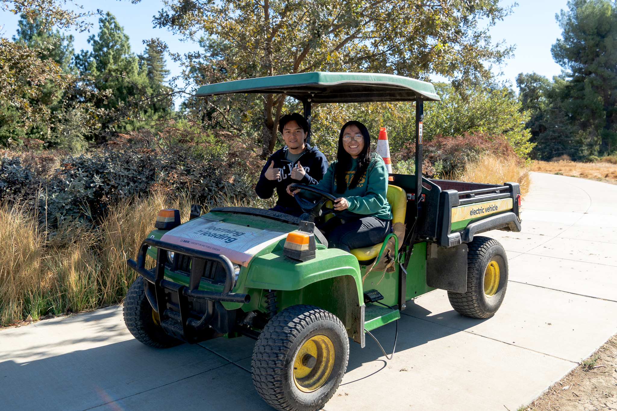 Two Arboretum Ambassador interns pose, smiling at the camera while in a cart in the Arboretum