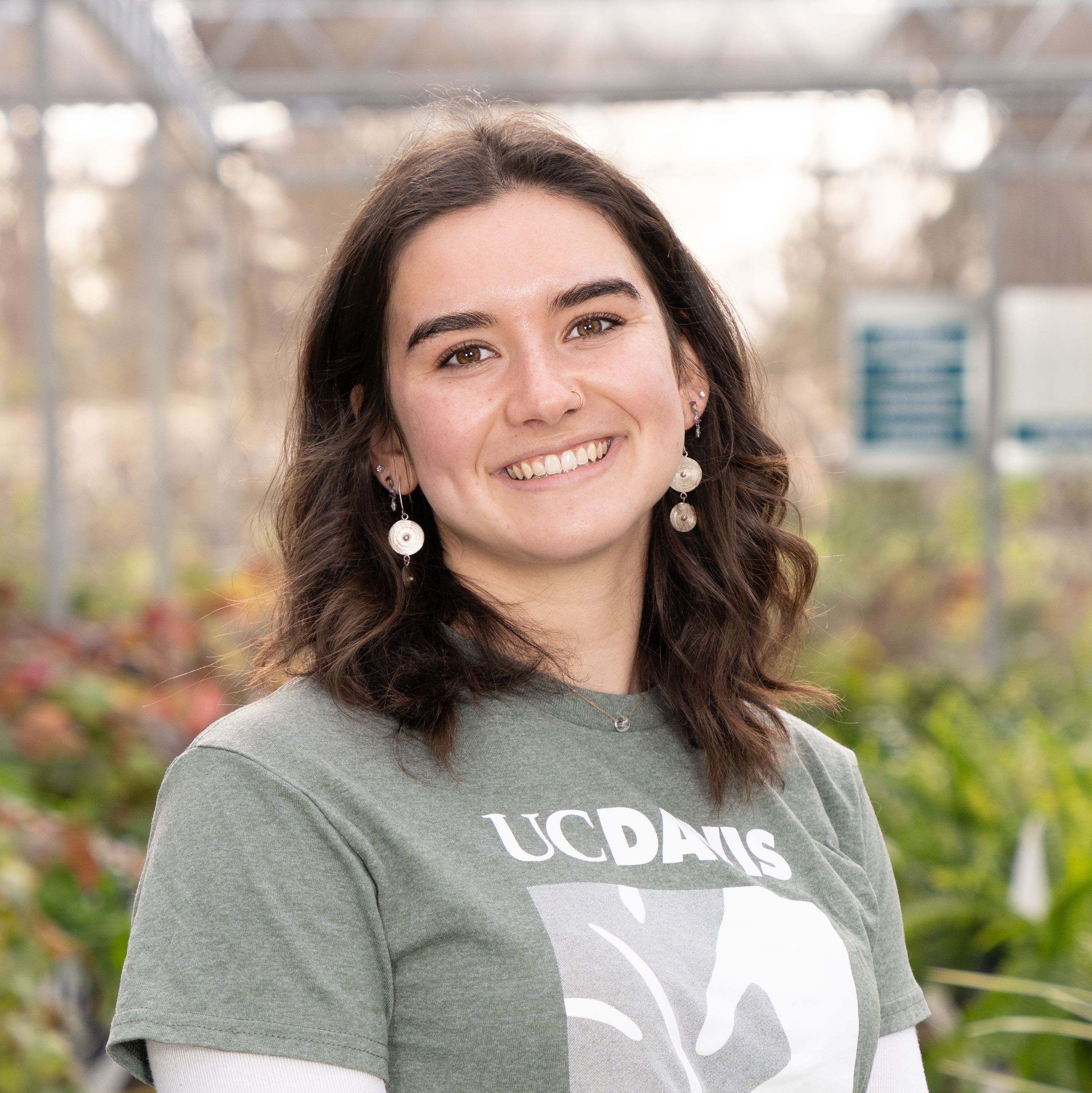 Enola Lagrave smiles among rows of plants in the Arboretum Teaching Nursery