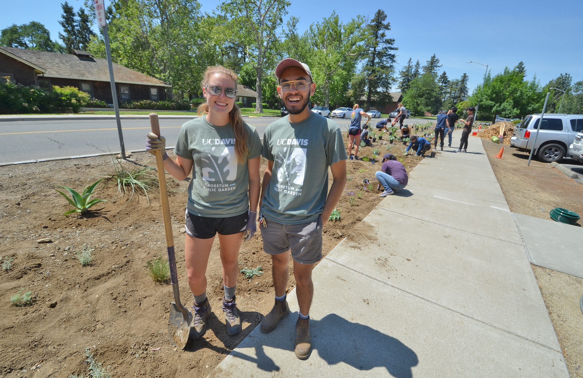 Students smiling outdoors with a shovel.