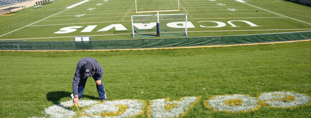 Image of staff from UC Davis Grounds and Landscape Services' sports turf team spray painting the football field.