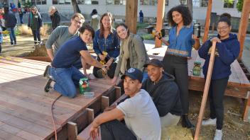 In the foreground, several students smile, pausing while installing a deck 