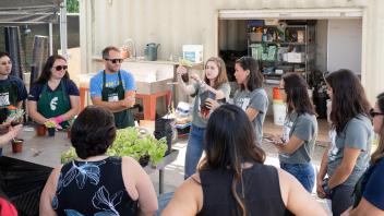 A dozen people, including several student interns, stand in the Arboretum Teaching Nursery as a student intern leads a discussion.