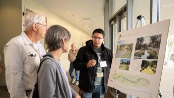 A student intern presents a poster on the Arboretum waterway enhancement program to two people.
