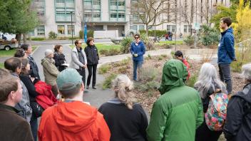 Just south of Shields Library, a group of over a dozen people stand in a circle listening to someone speak.