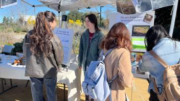 Three people gather around an Arboretum and Public Garden exhibit at Biodiversity Museum Day
