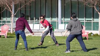A Learning by Leading student intern plays a game on the grass with two visitors 