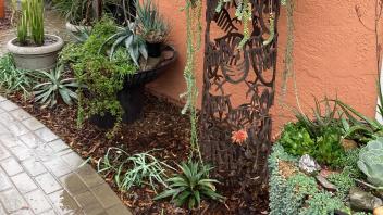 Container plantings alongside the side of a house, including a metal, sculptural container
