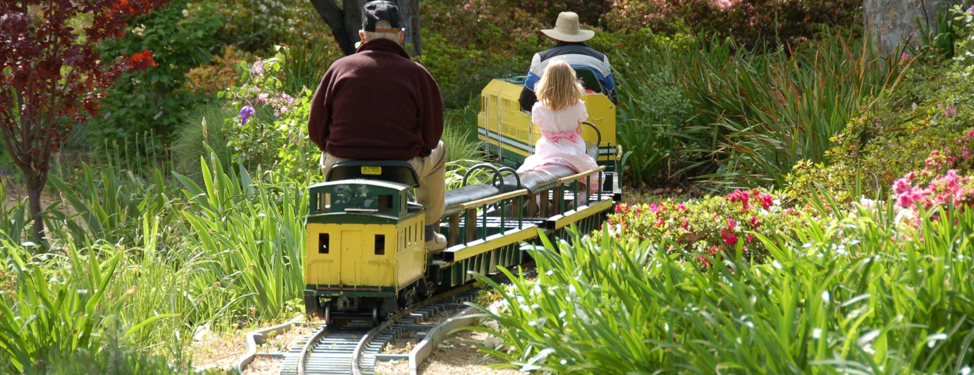 Image of two adults and a child on small train winding through a garden.