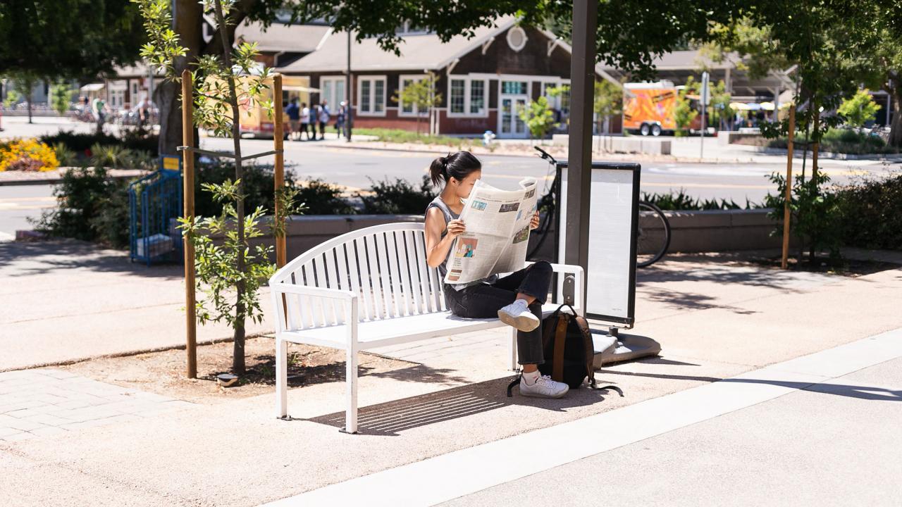 person reading the newspaper on a bench