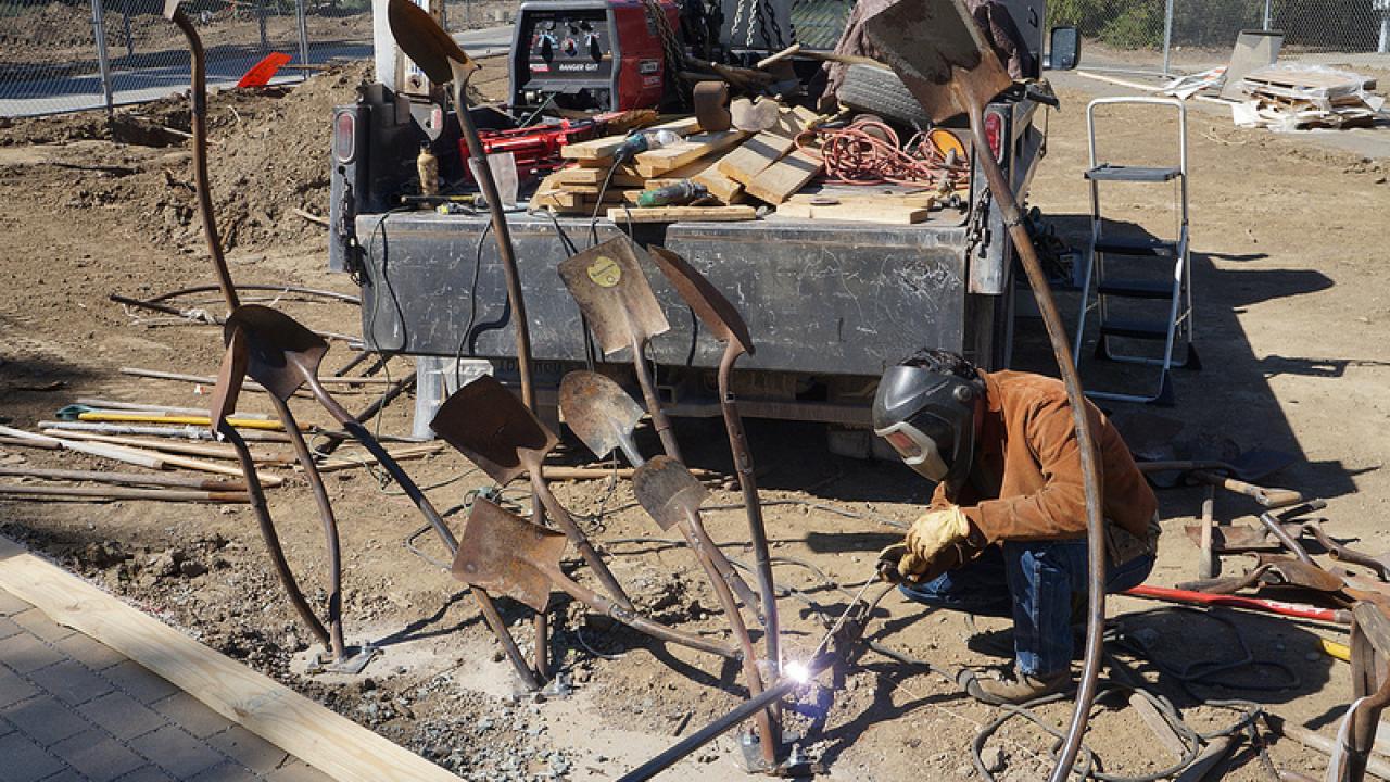 person building sculpture out of old shovels