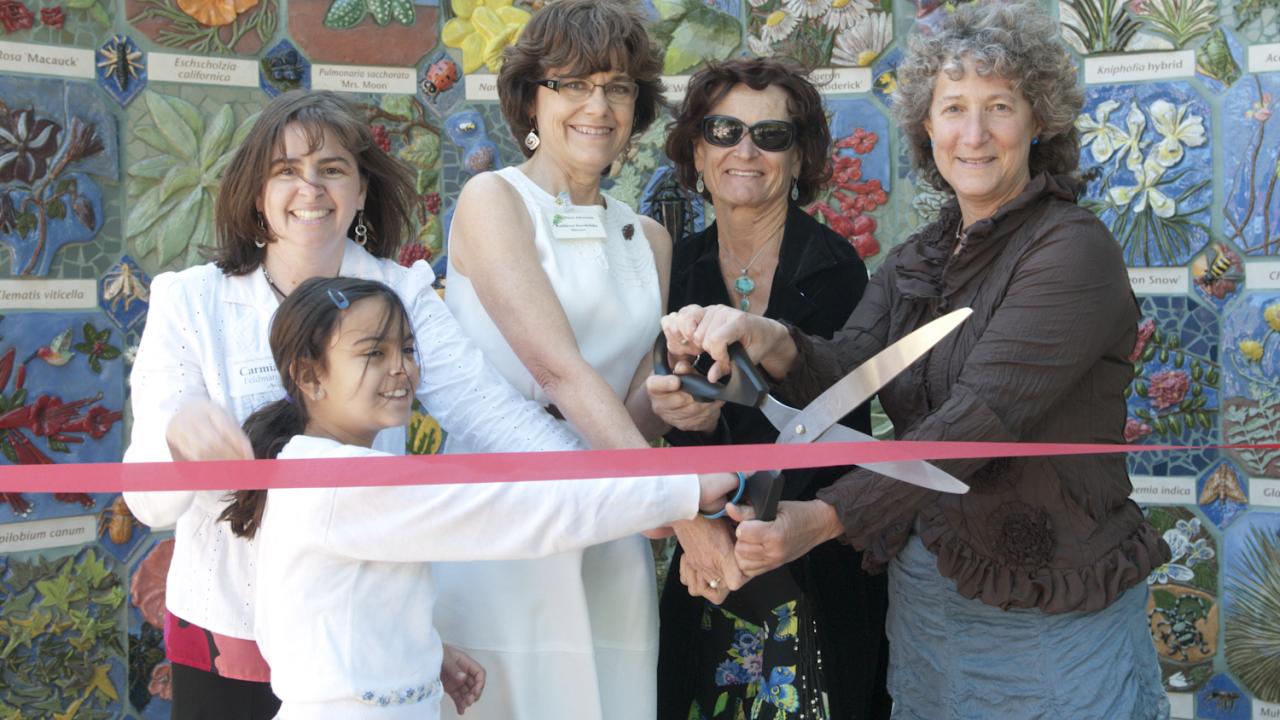 Group of people cutting ribbon in front of the mosaic mural of the Nature's Gallery Court.