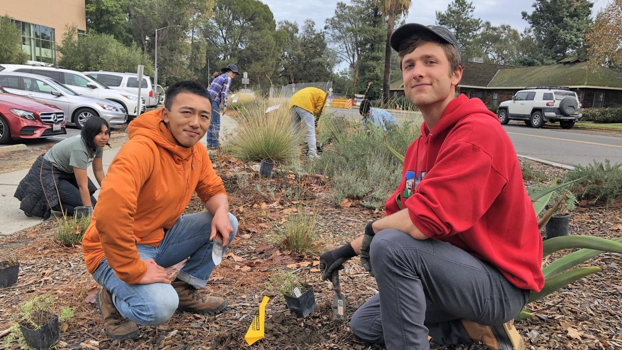 Program co-coordinators Chris Huang (left) and Cameron Long, who each have year of experience in the program, helped direct and guide the interns as they filled in the landscape along La Rue Road. Program co-coordinators Chris Huang and Cameron Long take a break from planting a new plant to pose for a photo, kneeling with the landscape in the background.