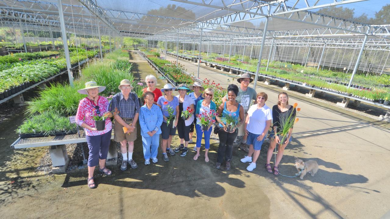 Image of a line of people standing in the foreground of a one-acre nursery filled to the brim with climate-appropriate plants; they are holding plants and smiling.