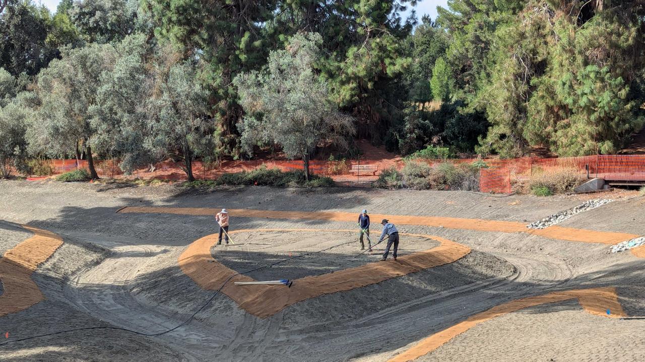 Three people work in a drained Arboretum Waterway