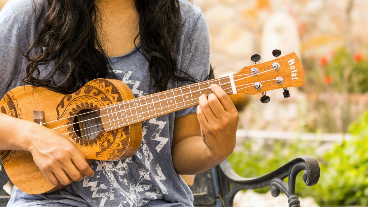 Person sits outdoors playing ukelele 