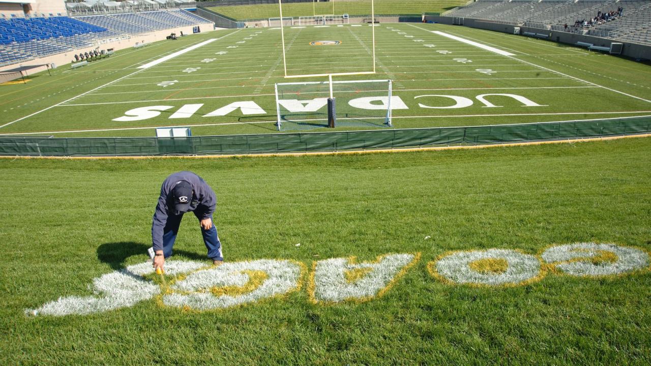 Groundskeeper paints "Go Ags" on grass near the UC Davis football field