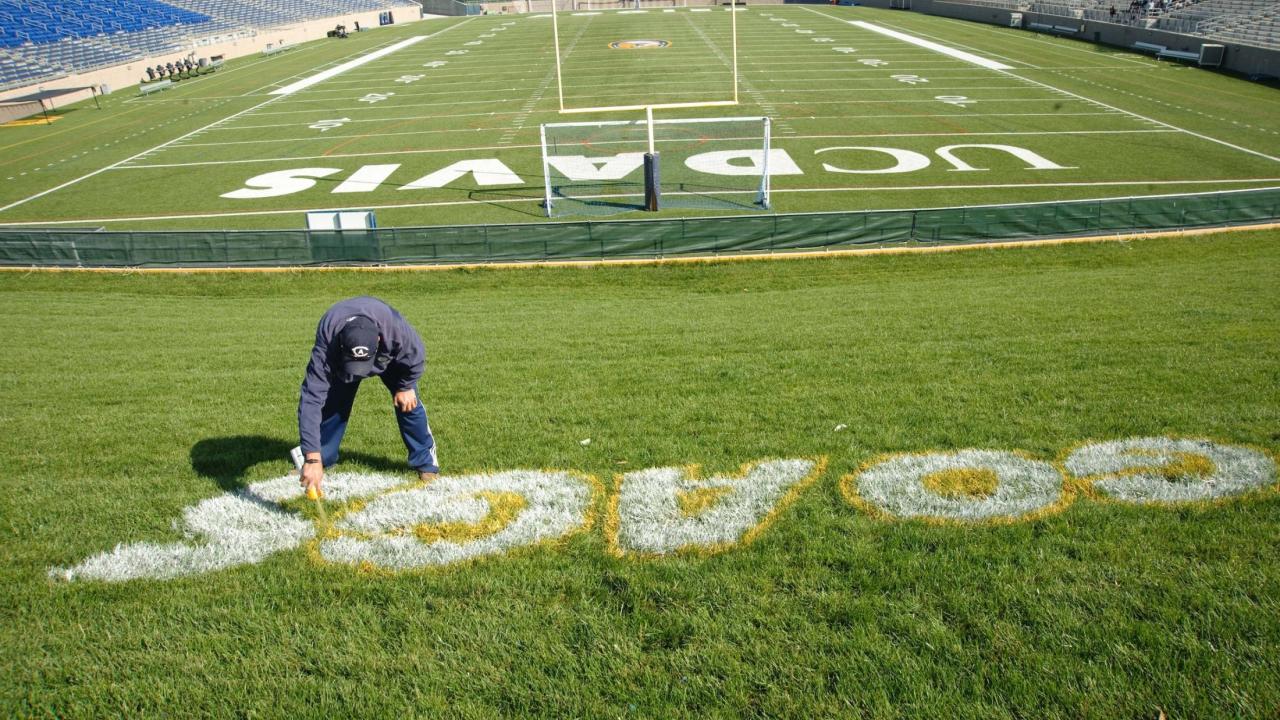Groundskeeper paints "Go Ags" on grass near the UC Davis football field