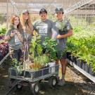 Four Arboretum student interns stand in the Arboretum Teaching Nursery, posing between two aisles of vibrant leafy plants