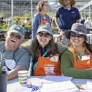 An Arboretum volunteer and two staff members smile, sitting at a table at an Arboretum Plant Sale