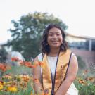 Terilyn Wong smiles, kneeling among flowers and wearing a UC Davis stole